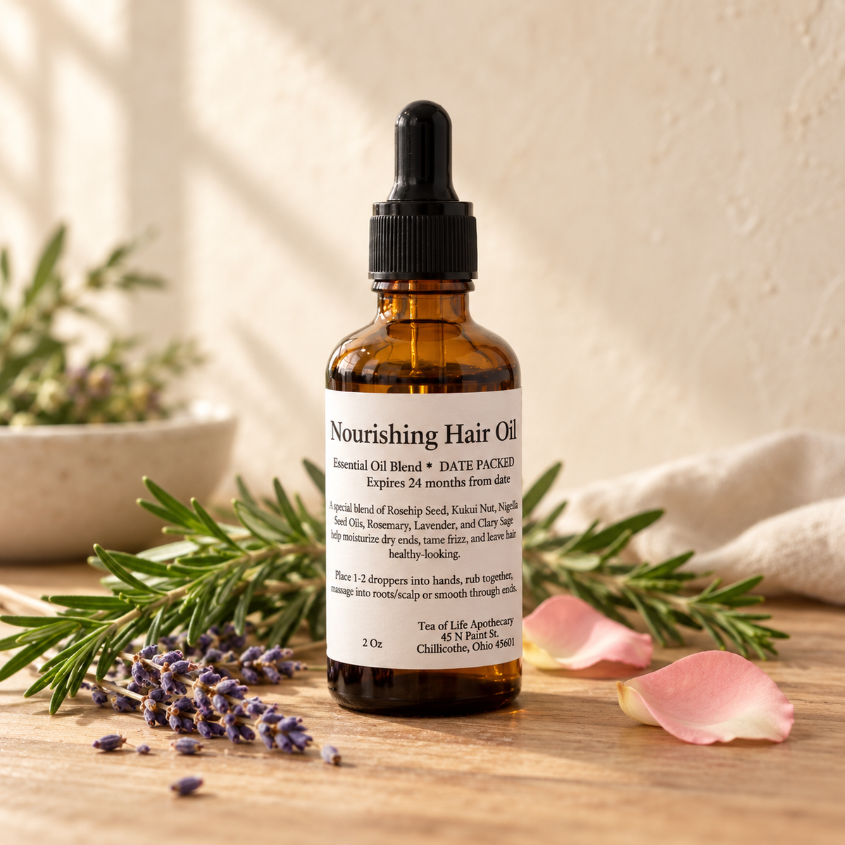 Tea of Life Apothecary Nourishing Hair Oil in a 2-ounce amber dropper bottle, styled with rosemary, lavender, and rose petals.