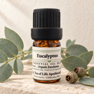 Tea of Life Apothecary Organic Eucalyptus Essential Oil in a 5 mL amber glass bottle, displayed with blue-green eucalyptus leaves and natural seed pods.