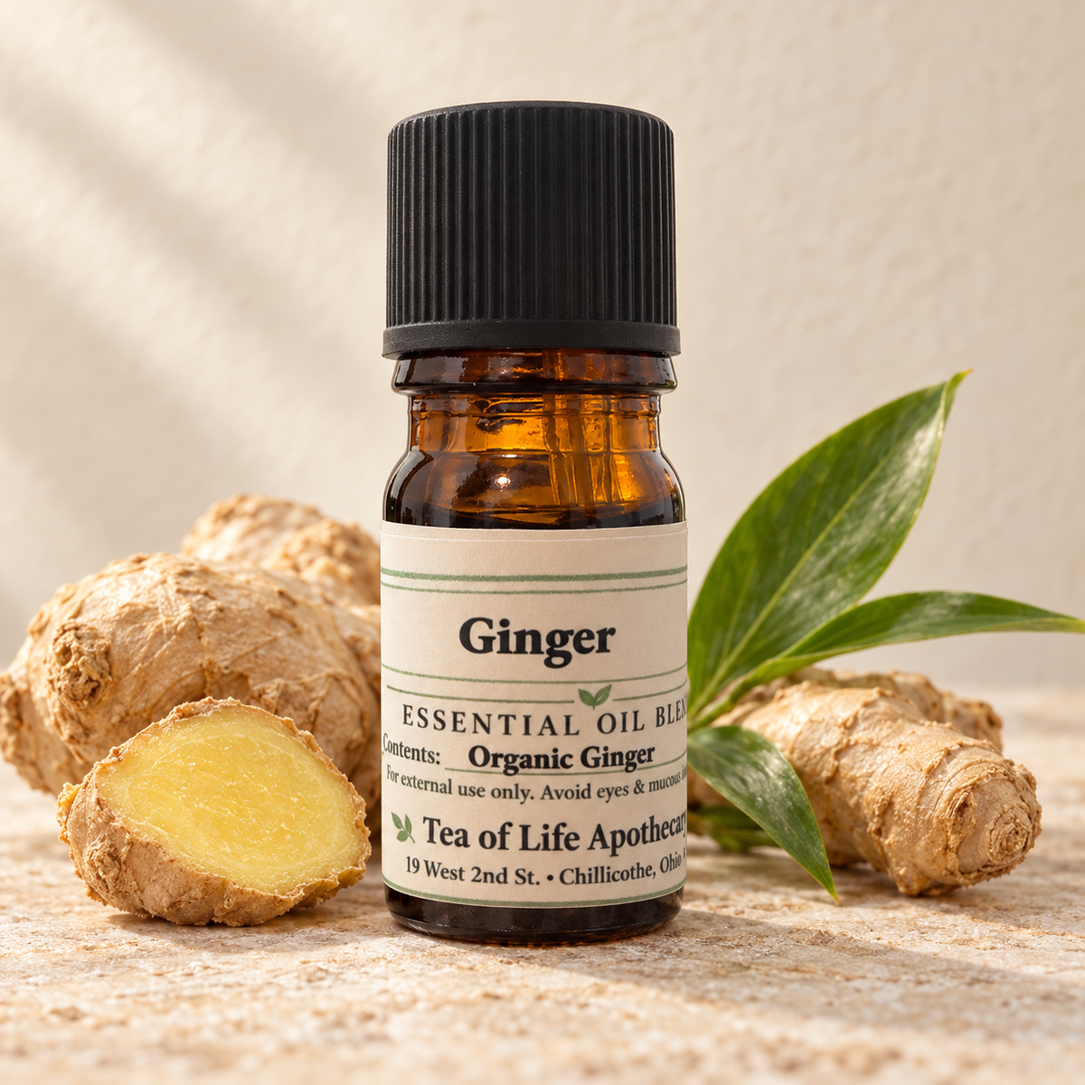 Tea of Life Apothecary Organic Ginger Essential Oil in a 5 mL amber glass bottle, displayed with fresh ginger root, a cut ginger slice and green leaves.