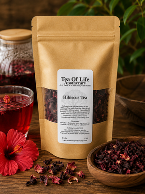 Tea of Life Apothecary Hibiscus Tea displayed with vibrant dried hibiscus petals, fresh hibiscus flowers, and a glass of deep ruby-red herbal tea on a rustic wooden table. This naturally caffeine-free herbal tea offers a refreshing tart, cranberry-like flavor that can be enjoyed hot or iced.