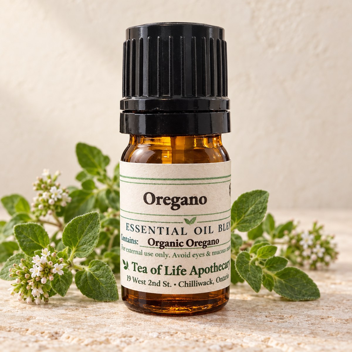 Tea of Life Apothecary Organic Oregano Essential Oil in a 5 mL amber glass bottle, displayed with fresh oregano leaves and delicate white blossoms.