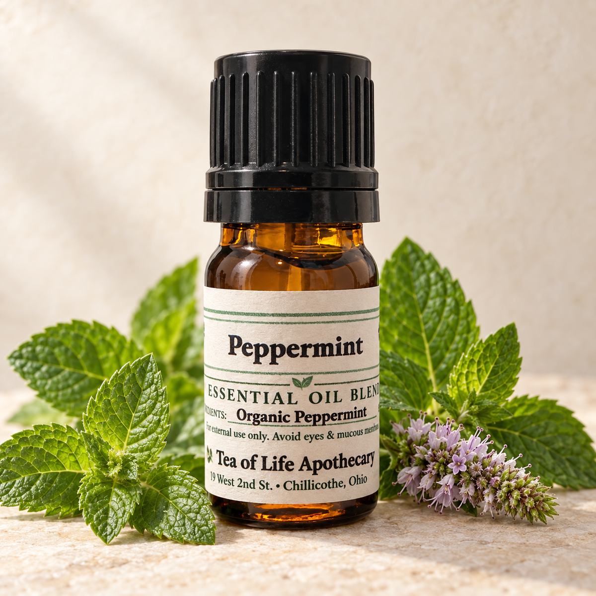 Tea of Life Apothecary Organic Peppermint Essential Oil in a 5 mL amber glass bottle, displayed with fresh peppermint leaves and flowering mint sprigs.