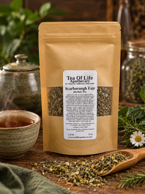 Tea of Life Apothecary Scarborough Fair Herbal Tea in a kraft pouch with a steaming cup of herbal tea, loose herbs, chamomile flowers, rosemary, and a rustic teapot in a cozy countryside setting.