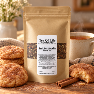Tea of Life Apothecary Snickerdoodle Herbal Tea displayed with a warm cup of tea, cinnamon sticks, and freshly baked cinnamon-sugar snickerdoodle cookies.