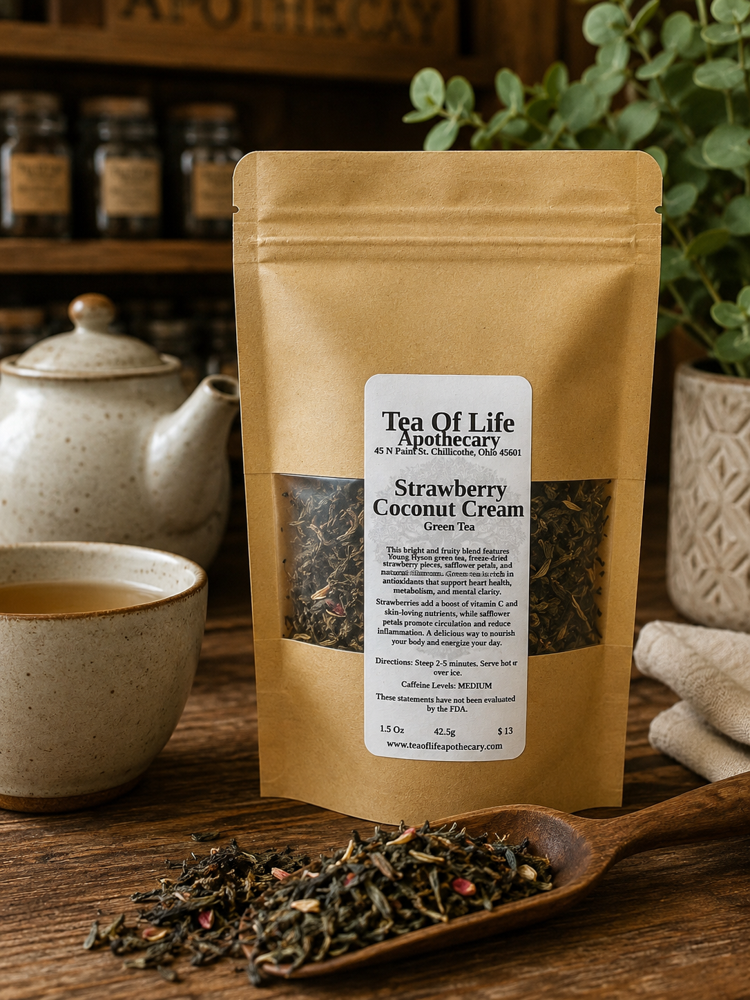 Tea of Life Apothecary Strawberry Coconut Cream Green Tea in a resealable kraft pouch displayed beside a warm cup of brewed green tea and loose tea leaves on a rustic wooden table, featuring a tropical strawberry and coconut flavored loose-leaf green tea blend.