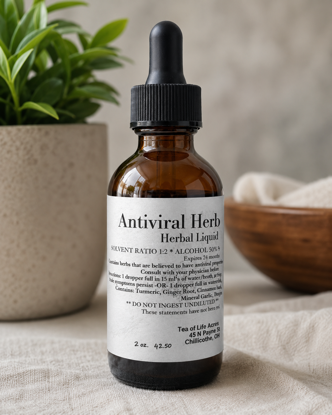 Amber glass antiviral herbal tincture bottle with dropper from Tea of Life Apothecary displayed on neutral fabric beside a green plant in a natural wellness setting.