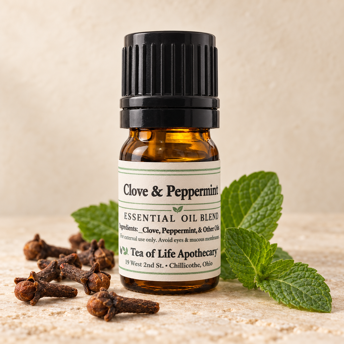 Tea of Life Apothecary Clove and Peppermint Essential Oil Blend in a 5 mL amber bottle, surrounded by whole cloves and fresh peppermint leaves.