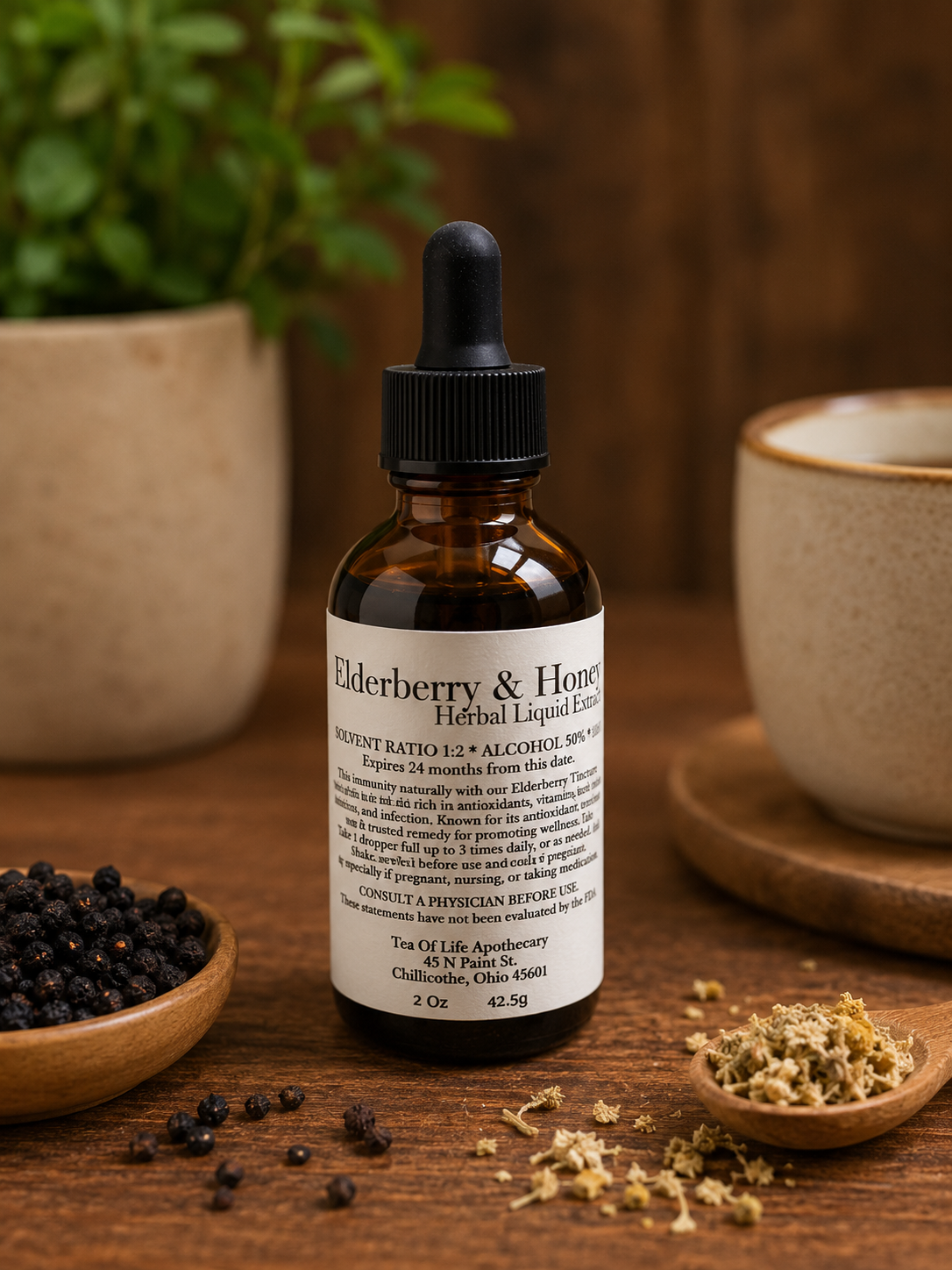 Tea of Life Apothecary Elderberry & Honey Herbal Liquid Extract tincture bottle displayed on a rustic wooden table with dried elderberries and herbs in a warm apothecary setting.