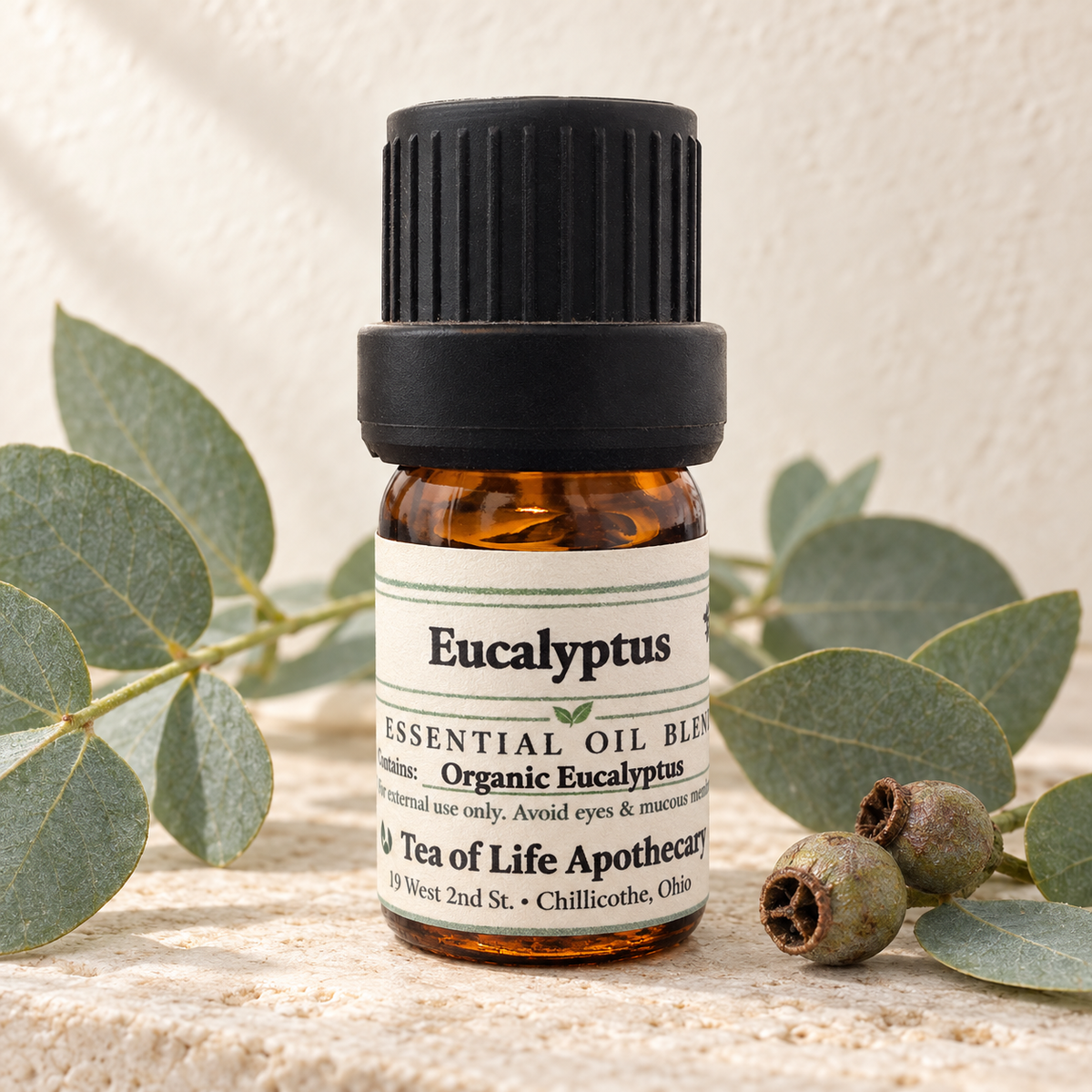 Tea of Life Apothecary Organic Eucalyptus Essential Oil in a 5 mL amber glass bottle, displayed with blue-green eucalyptus leaves and natural seed pods.