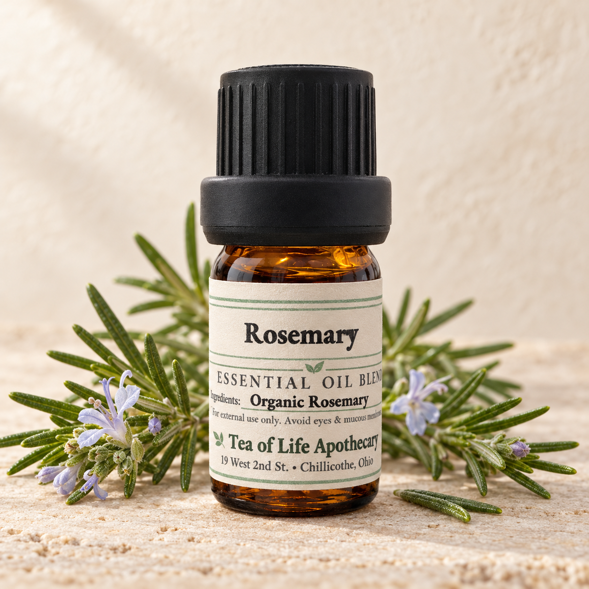 Tea of Life Apothecary Organic Rosemary Essential Oil in a 5 mL amber glass bottle, displayed with fresh rosemary sprigs and pale blue flowers.