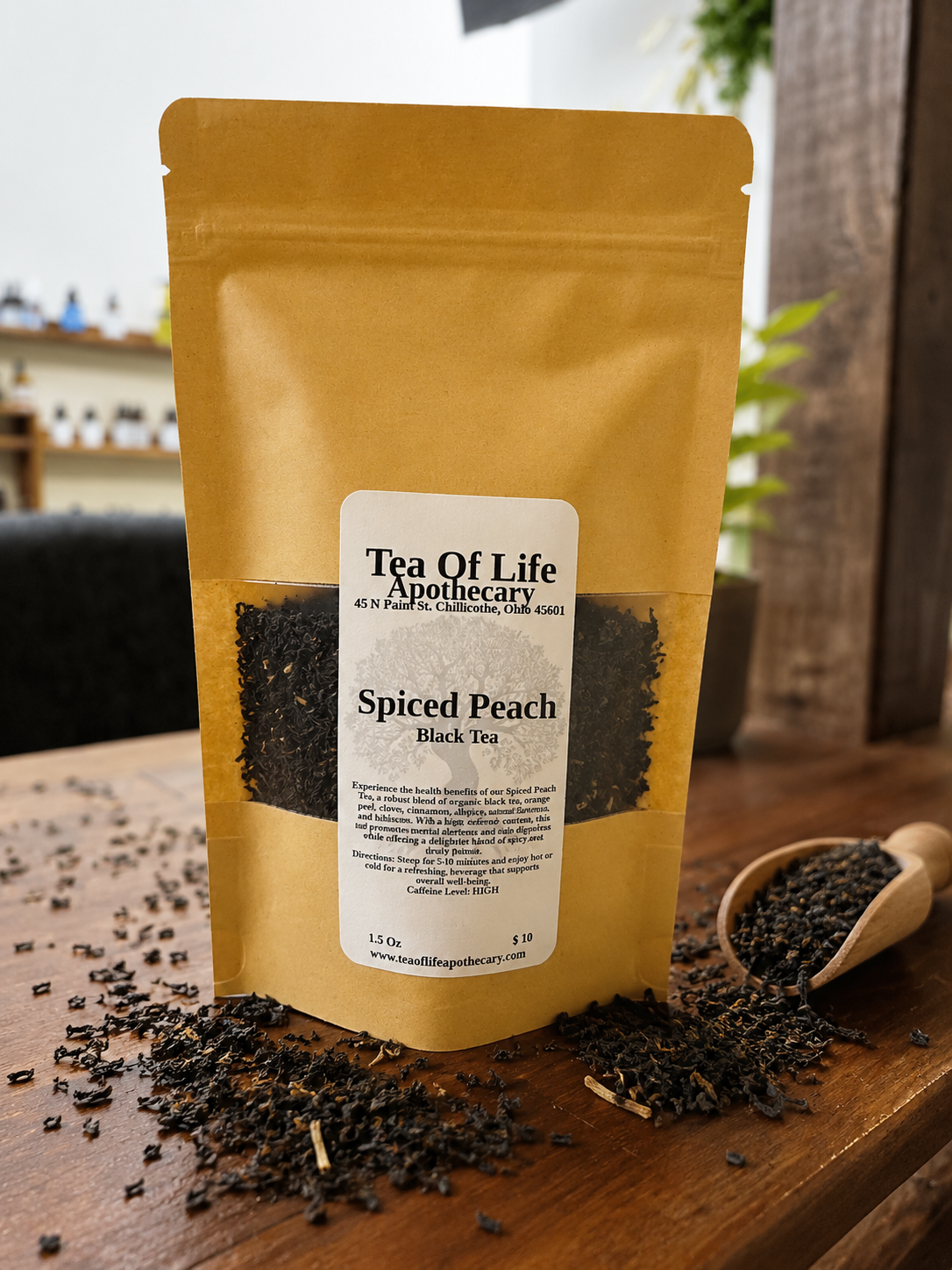 Tea of Life Apothecary Spiced Peach Black Tea loose leaf tea in a kraft stand-up pouch with black tea leaves scattered around the package on a rustic wooden table, showcasing a premium handcrafted flavored black tea blend.