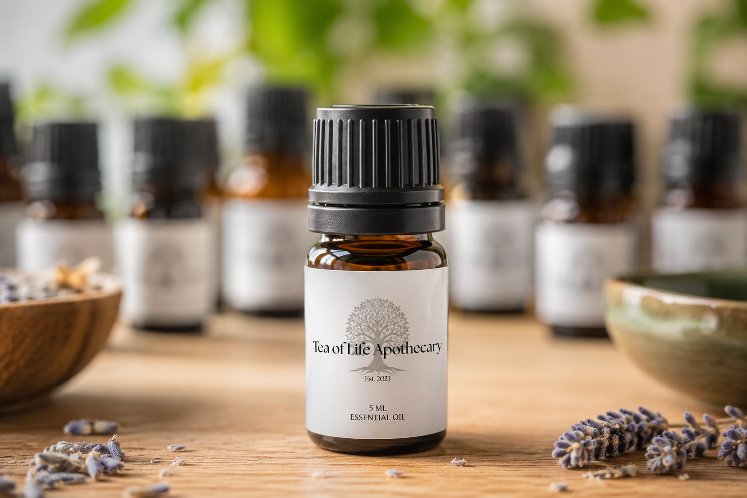 Tea of Life Apothecary 5 mL amber essential oil bottle with branded label displayed on a wooden surface with softly blurred essential oil bottles in the background, representing our handcrafted botanical essential oil collection.