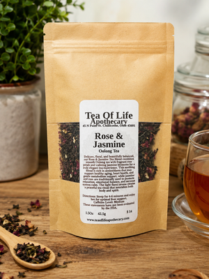 Tea of Life Apothecary Rose & Jasmine Oolong Tea in a kraft stand-up pouch displayed on a rustic wooden table beside a glass cup of tea, loose tea leaves, and greenery in a warm apothecary setting.