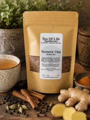 Tea of Life Apothecary Turmeric Chai Herbal Tea displayed with fresh ginger root, cinnamon sticks, turmeric powder, cardamom pods, black peppercorns, and a steaming cup of chai tea on a rustic wooden table, highlighting the warm, aromatic ingredients of this caffeine-free herbal blend.
